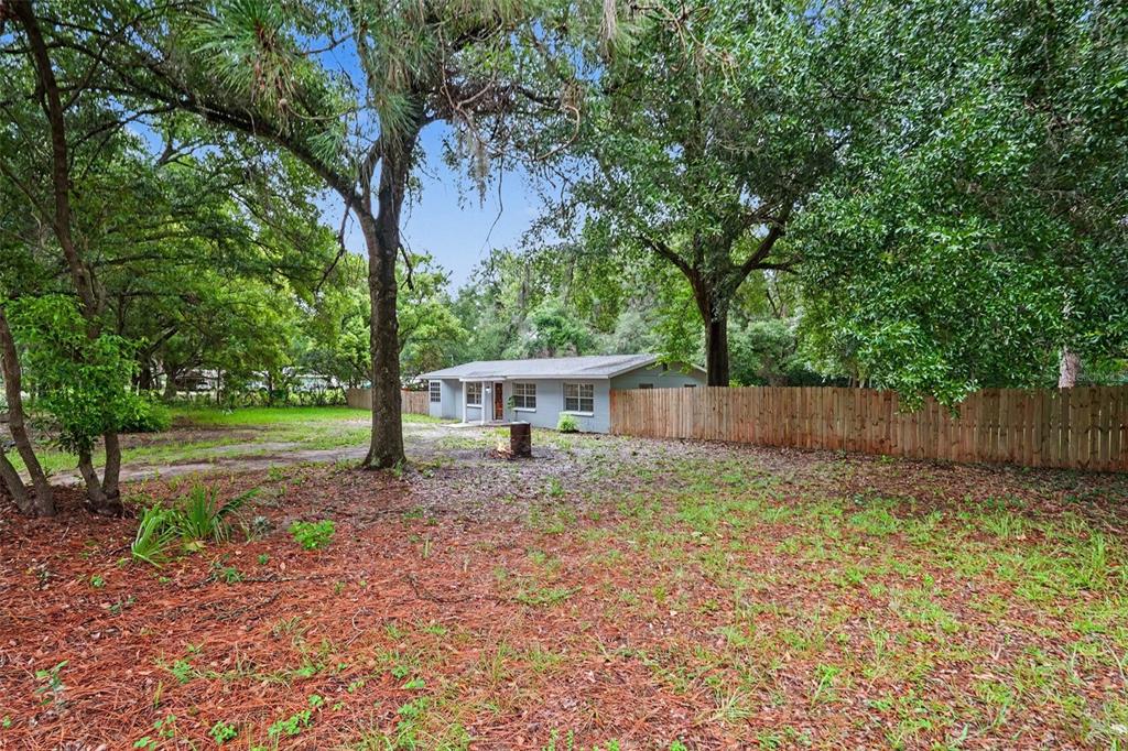 A single-story house sits behind a wooden fence in a yard with many trees — 5328 LANTANA STREET, ZEPHYRHILLS, FL