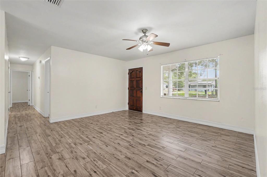 An empty living room features light wood-look tile flooring, white walls, and a ceiling fan — 5328 LANTANA STREET, ZEPHYRHILLS, FL