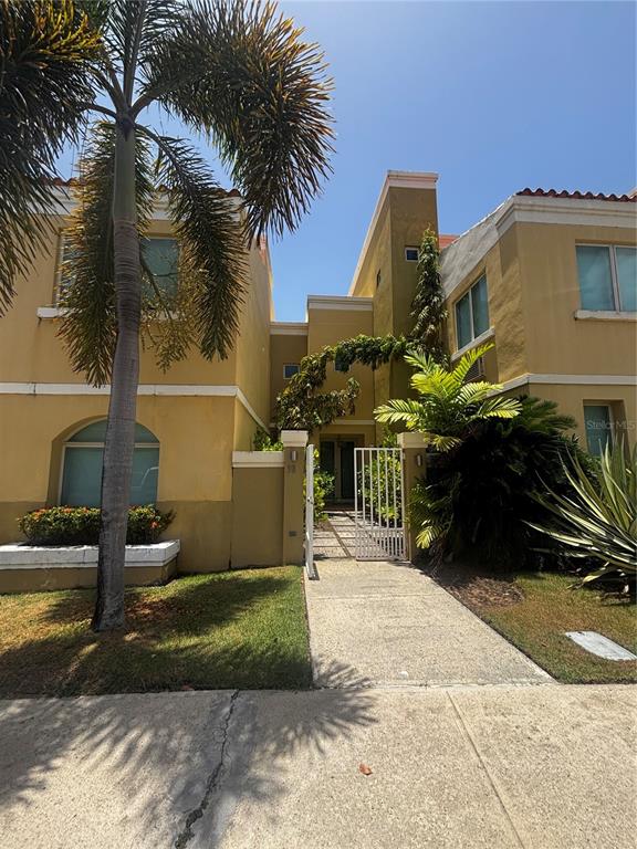 A two-story yellow stucco building features a palm tree, a gated entrance, and landscaping — 98 VIA POSITANO UNIT 98, HUMACAO, PR