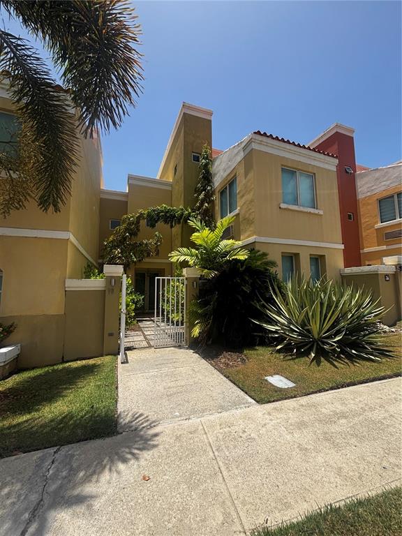 A two-story yellow stucco townhouse features a gated entryway, palm trees, and landscaping — 98 VIA POSITANO UNIT 98, HUMACAO, PR
