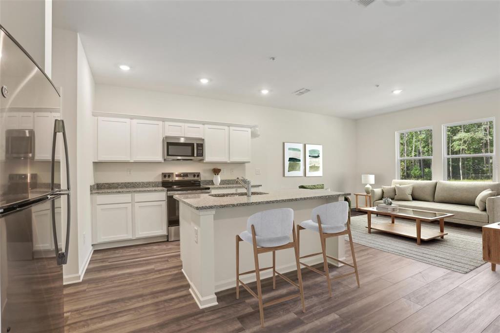 This open-concept kitchen and living area features white cabinetry, a kitchen island, and wood flooring — 2587 GREY HAWK DRIVE,, KISSIMMEE, FL