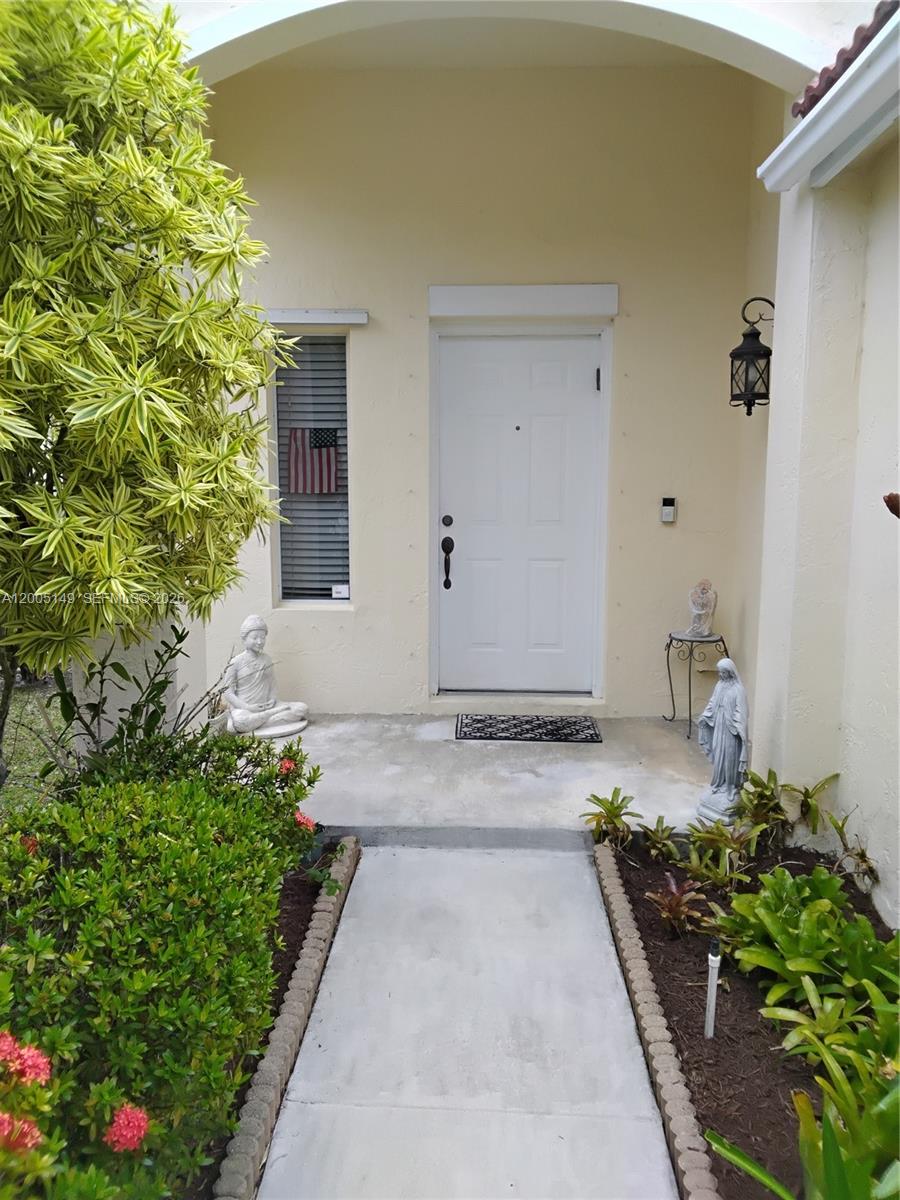 A concrete walkway leads to a white front door with a side window and statues — 519 Talavera Rd, Weston FL 33326, WESTON, FL