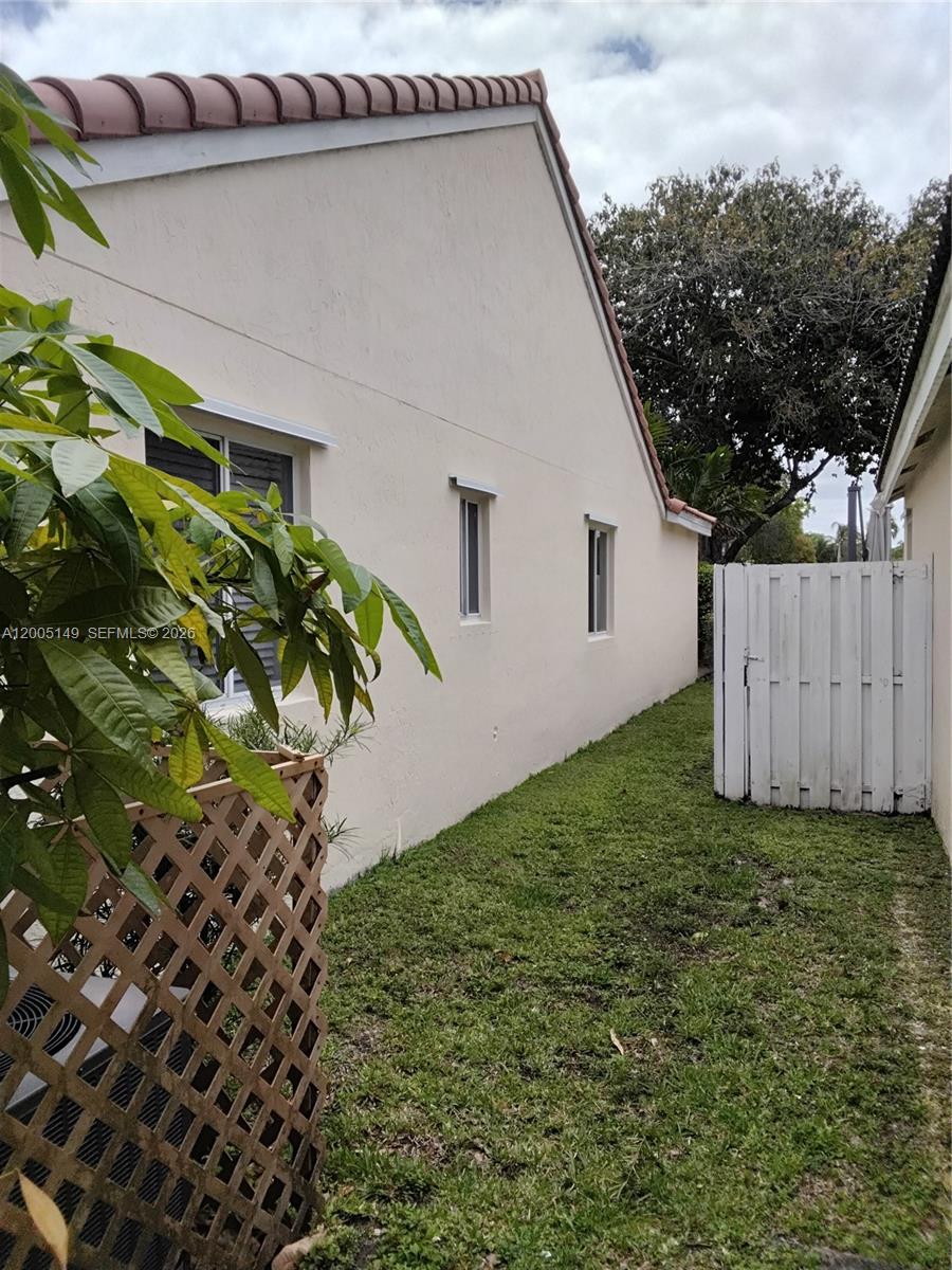 A side view of a beige house exterior with a white fence and lawn — 519 Talavera Rd, Weston FL 33326, WESTON, FL