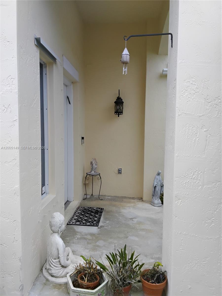 A covered entryway features a concrete floor, a wall-mounted lantern, and several decorative statues — 519 Talavera Rd, Weston FL 33326, WESTON, FL
