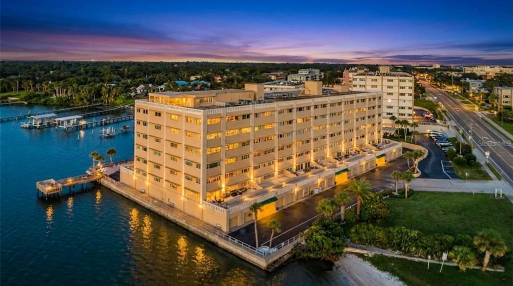 An aerial view of a multi-story apartment building situated on a waterfront lot at sunset — 100 BLUFF VIEW DRIVE UNIT 604C, BELLEAIR BLUFFS, FL