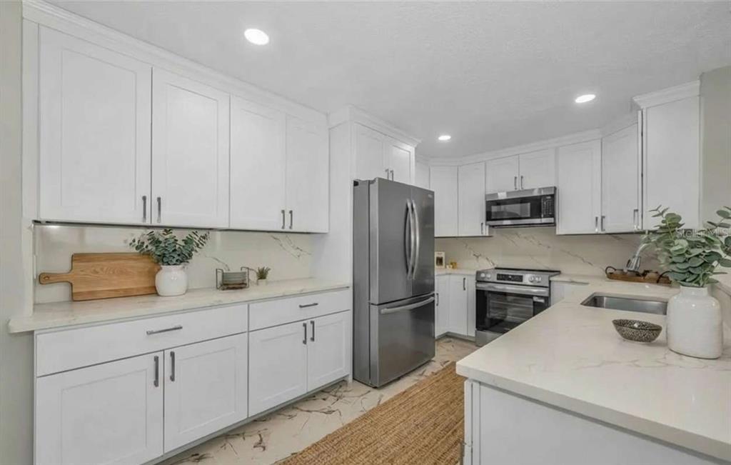 A modern kitchen featuring white cabinets, stainless steel appliances, and marble-look countertops — 100 BLUFF VIEW DRIVE UNIT 604C, BELLEAIR BLUFFS, FL