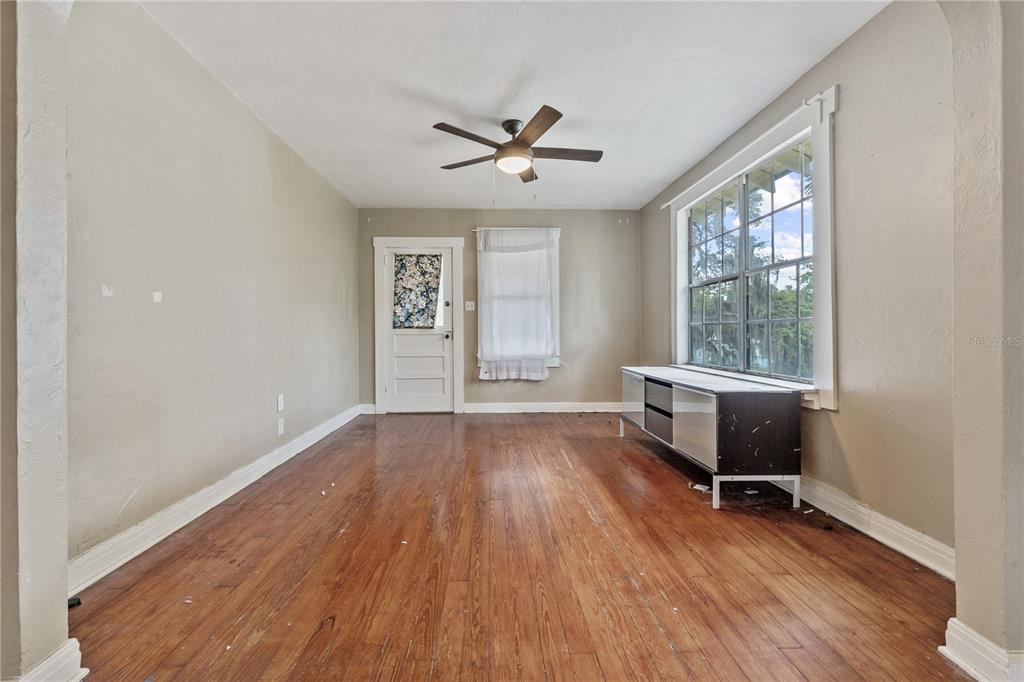 An empty room features hardwood floors, a ceiling fan, a window, and a white door — 5914 N OLA AVENUE, TAMPA, FL