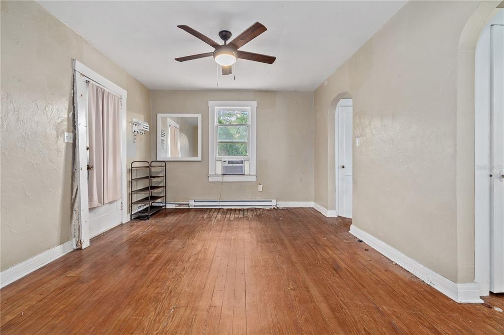 An empty room features hardwood floors, a ceiling fan, a window unit, and arched doorways — 5914 N OLA AVENUE, TAMPA, FL