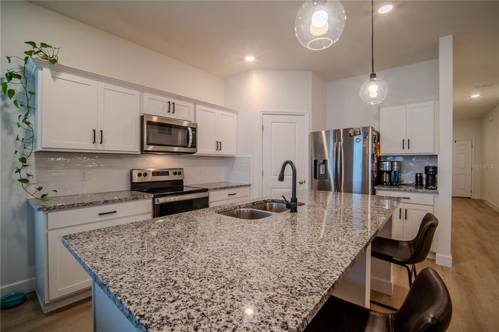 A modern kitchen with white cabinets and an island opens to a dining area — 5859 HERDER ROAD, ST CLOUD, FL