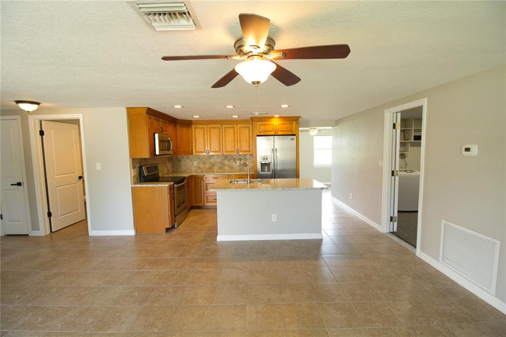 A kitchen with wood cabinets, granite countertops, and an island opens to a tiled room — 4632 SALVIA STREET, NEW PORT RICHEY, FL