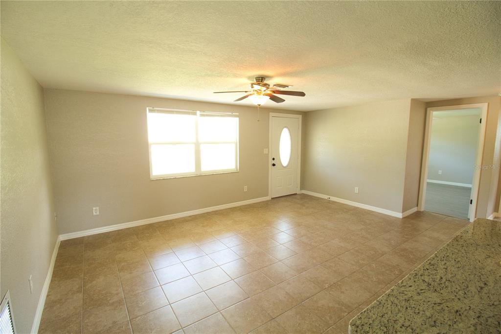 A living room with beige walls, tile flooring, a ceiling fan, and a front door — 4632 SALVIA STREET, NEW PORT RICHEY, FL