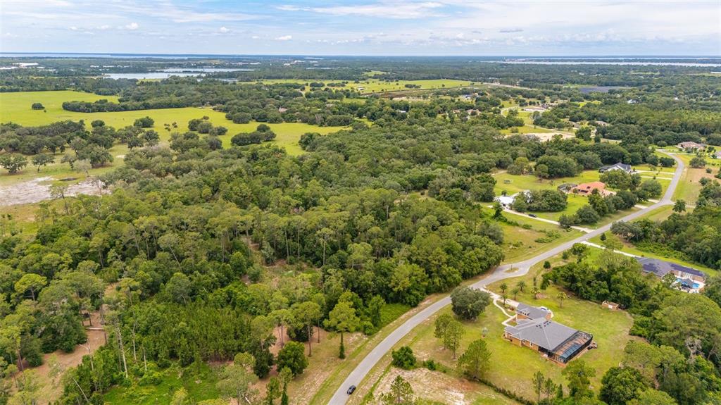 An aerial view shows a rural landscape with a paved road, scattered houses, and dense woods — 27037 GRAND OAK LANE, TAVARES, FL
