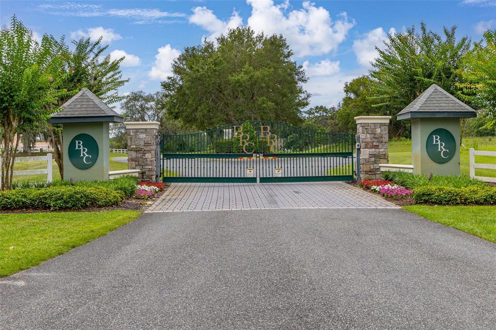 A gated entrance with stone pillars and green metal gates featuring a BRC logo — 27037 GRAND OAK LANE, TAVARES, FL