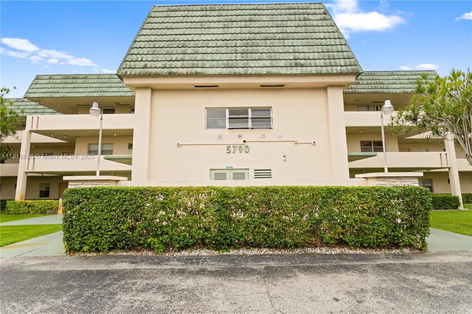 A low-rise apartment building features a green mansard roof and a manicured hedge in front — 5790 Stirling # 212, Hollywood FL 33021, HOLLYWOOD, FL