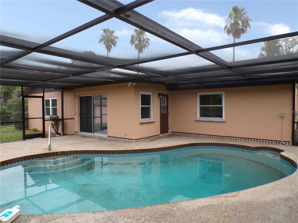 A swimming pool with a screened-in patio area sits behind a tan house — 1622 17TH STREET E, BRADENTON, FL