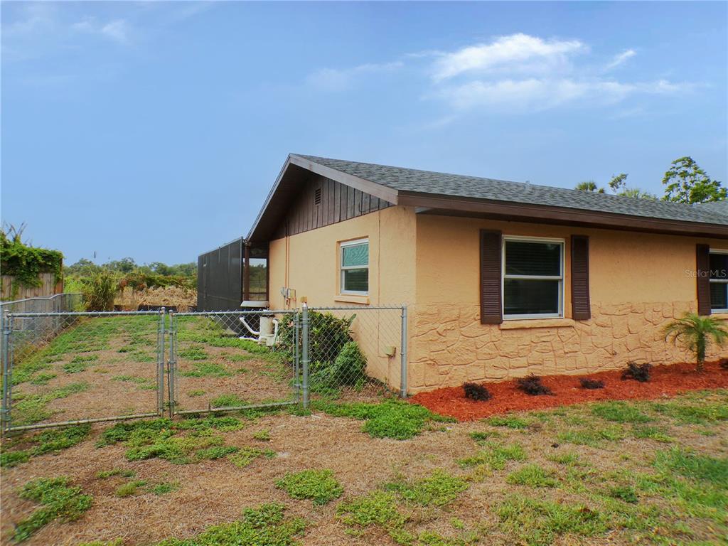 A side view of a tan house with stone siding and a chain-link fence — 1622 17TH STREET E, BRADENTON, FL