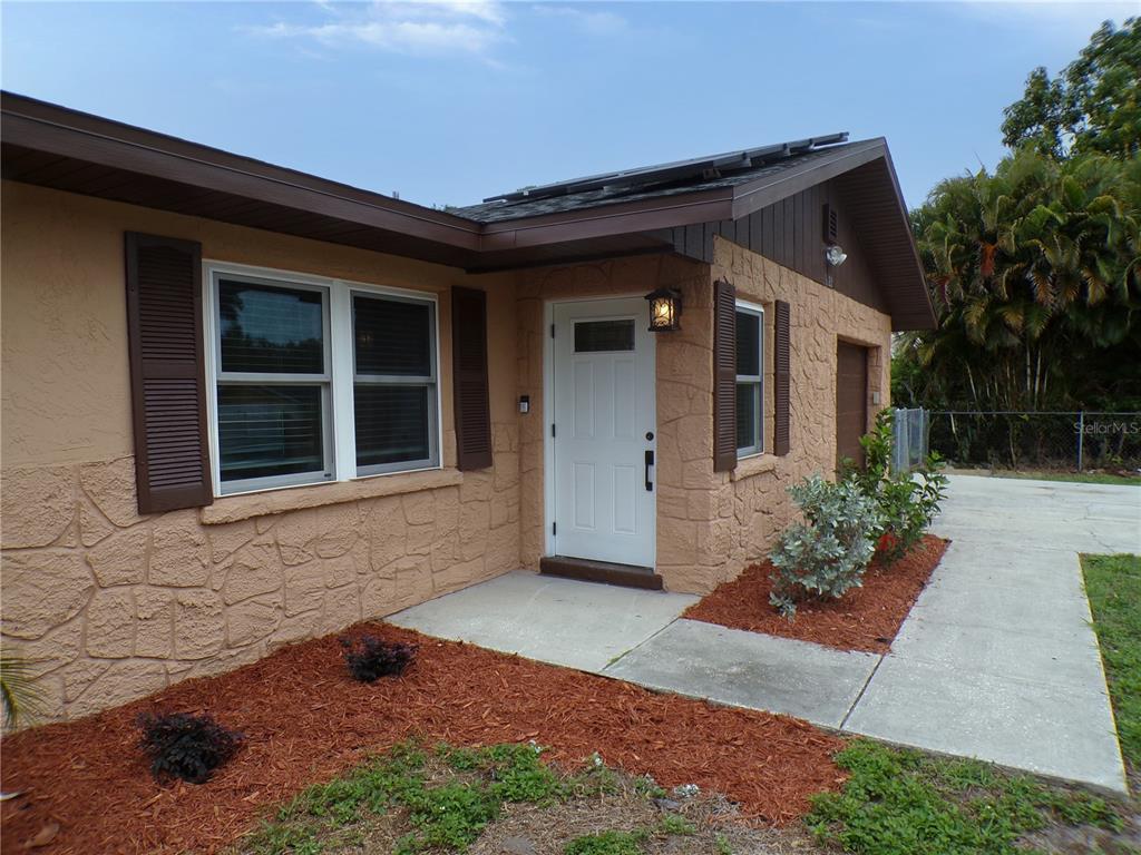 A tan house exterior features a white front door, stone-textured siding, and brown shutters — 1622 17TH STREET E, BRADENTON, FL
