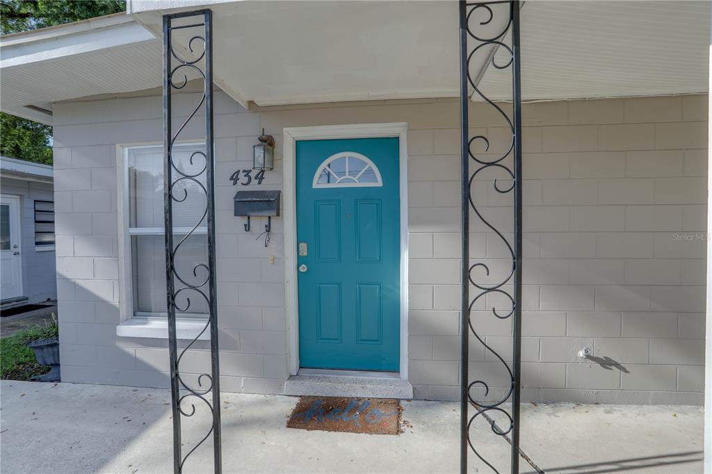 A teal front door with a decorative window sits on a gray concrete block exterior — 434 E ESTHER STREET, ORLANDO, FL