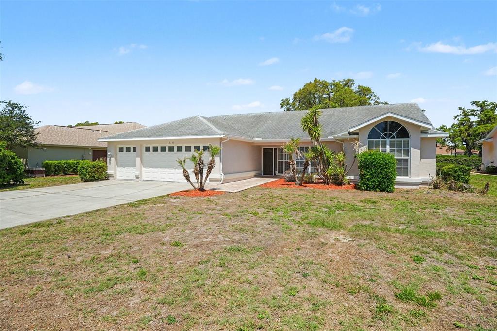 A single-story house with a two-car garage, light-colored stucco exterior, and a large arched window — 9389 FOX HOLLOW LANE, WEEKI WACHEE, FL
