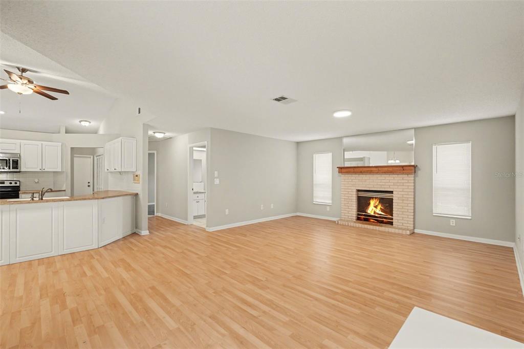 A living room with light wood floors, a brick fireplace, and an adjacent kitchen area — 9389 FOX HOLLOW LANE, WEEKI WACHEE, FL