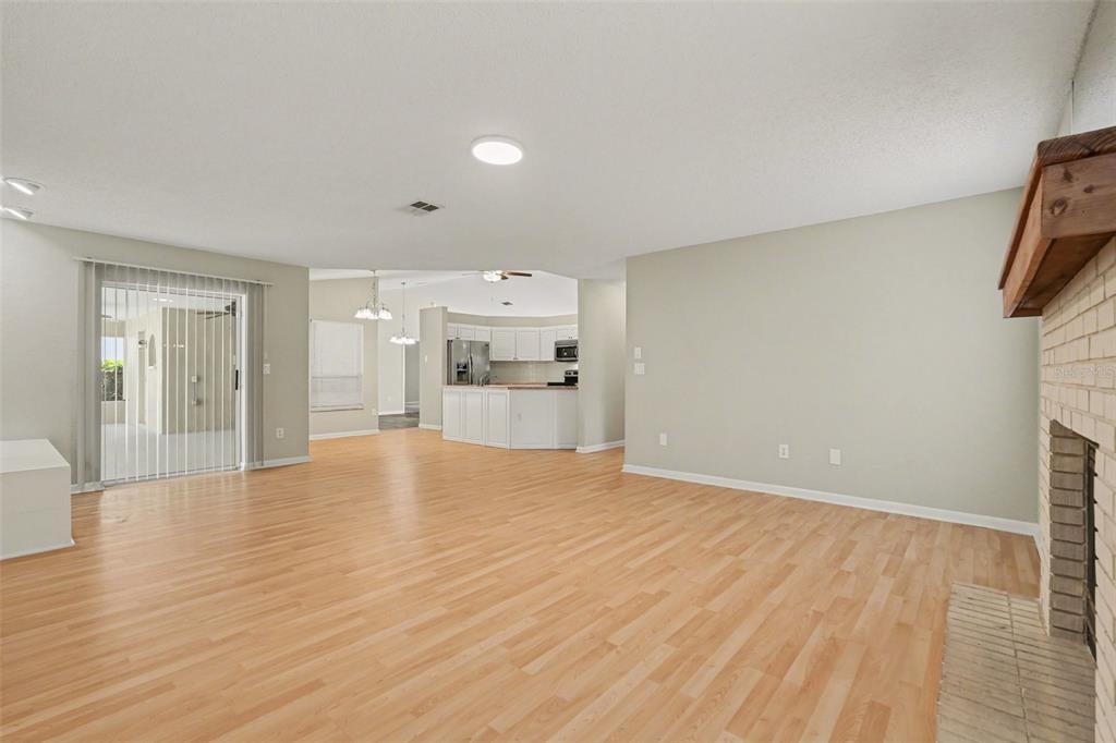 A spacious living room with light wood flooring, a brick fireplace, and an open kitchen — 9389 FOX HOLLOW LANE, WEEKI WACHEE, FL