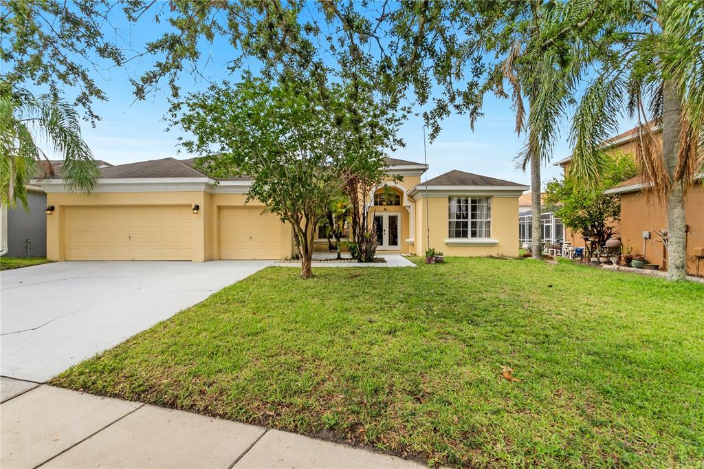 A single-story yellow house with a three-car garage and a front lawn with trees — 730 BRIDGEWAY BLVD, ORLANDO, FL