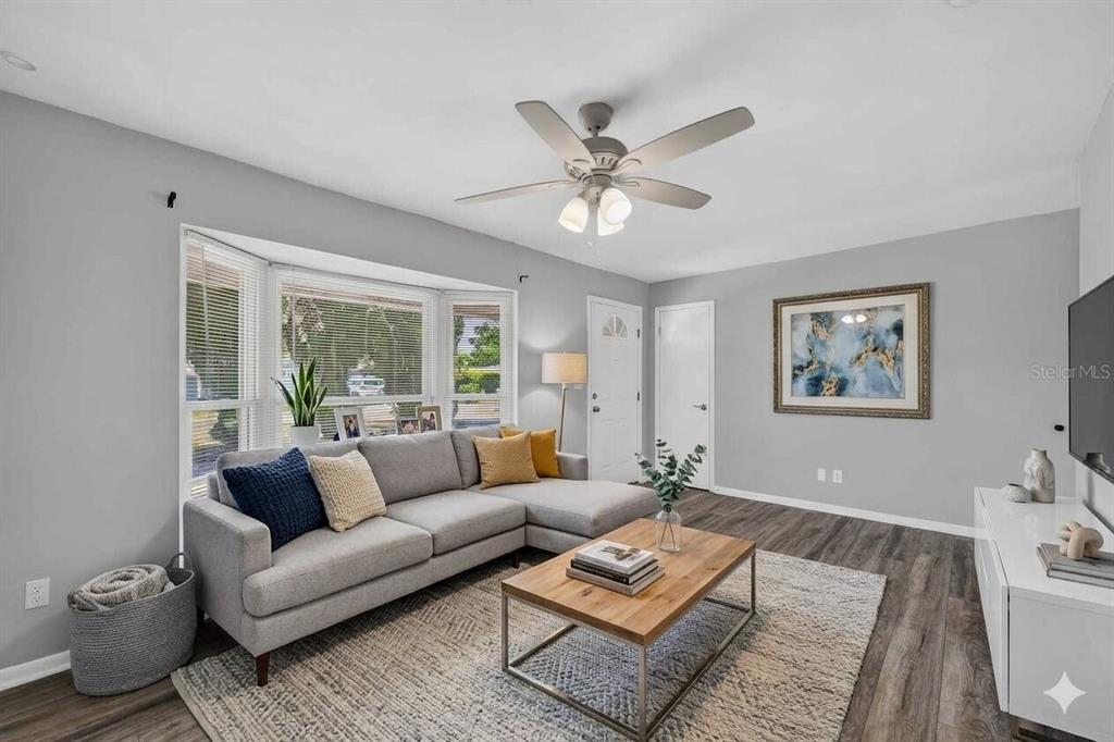 A living room features a gray sectional sofa, wood coffee table, and gray wood-look flooring — 10760 62ND AVENUE, SEMINOLE, FL