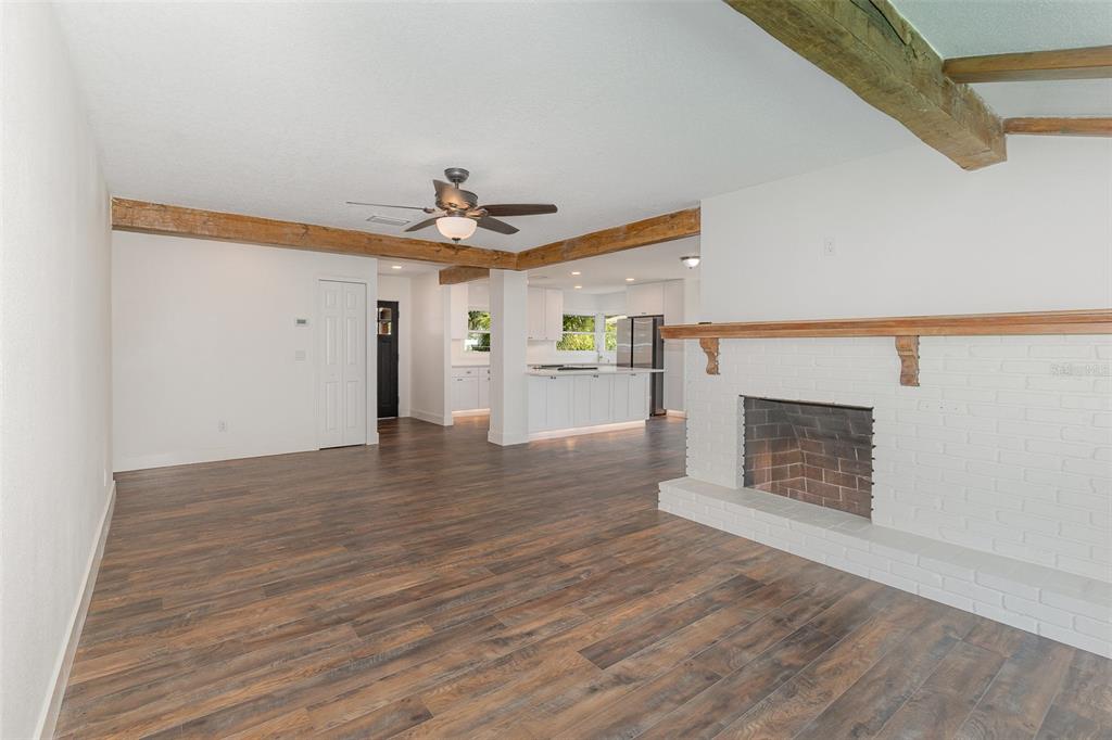 A living room with a white brick fireplace, wood beams, and wood-look flooring — 1770 ALGONQUIN TRAIL, MAITLAND, FL