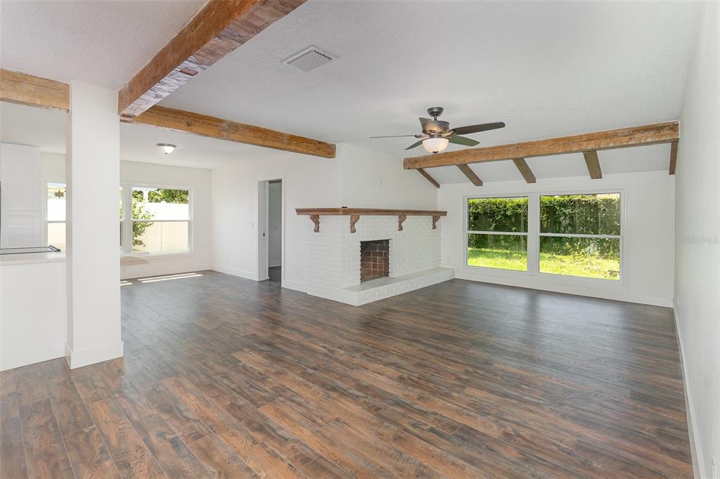 A living room with wood-look flooring, a white brick fireplace, and exposed ceiling beams — 1770 ALGONQUIN TRAIL, MAITLAND, FL