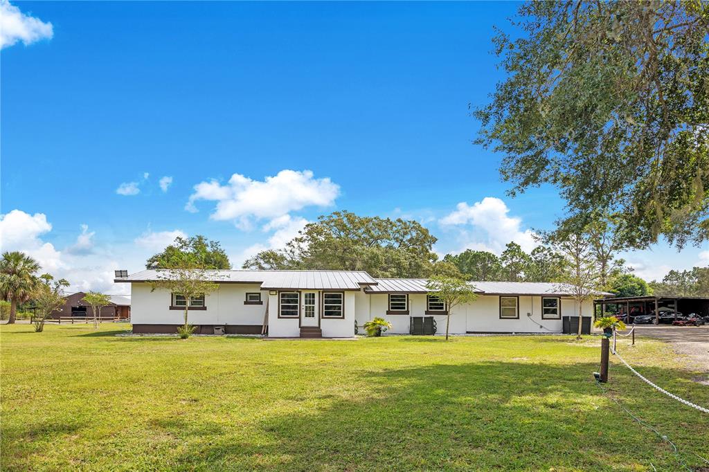 A white, single-story house with a metal roof sits on a large, grassy lawn — 32708 GERE LANE, SORRENTO, FL