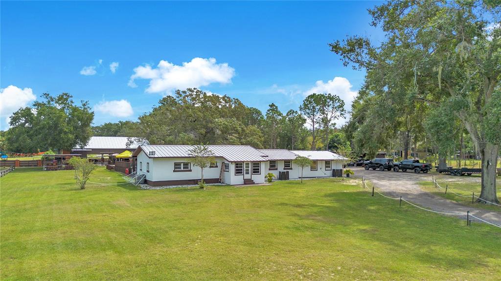 A long, white, single-story house with a metal roof sits on a large grassy lot — 32708 GERE LANE, SORRENTO, FL
