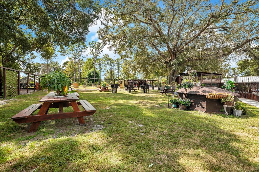 A grassy outdoor patio area features picnic tables, potted plants, and large shade trees — 32708 GERE LANE, SORRENTO, FL