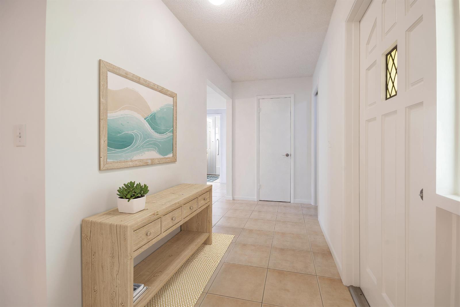 A tiled hallway features a light wood console table, a coastal wall print, and white doors — 18020 Palm Point Drive, Jupiter FL 33458, JUPITER, FL