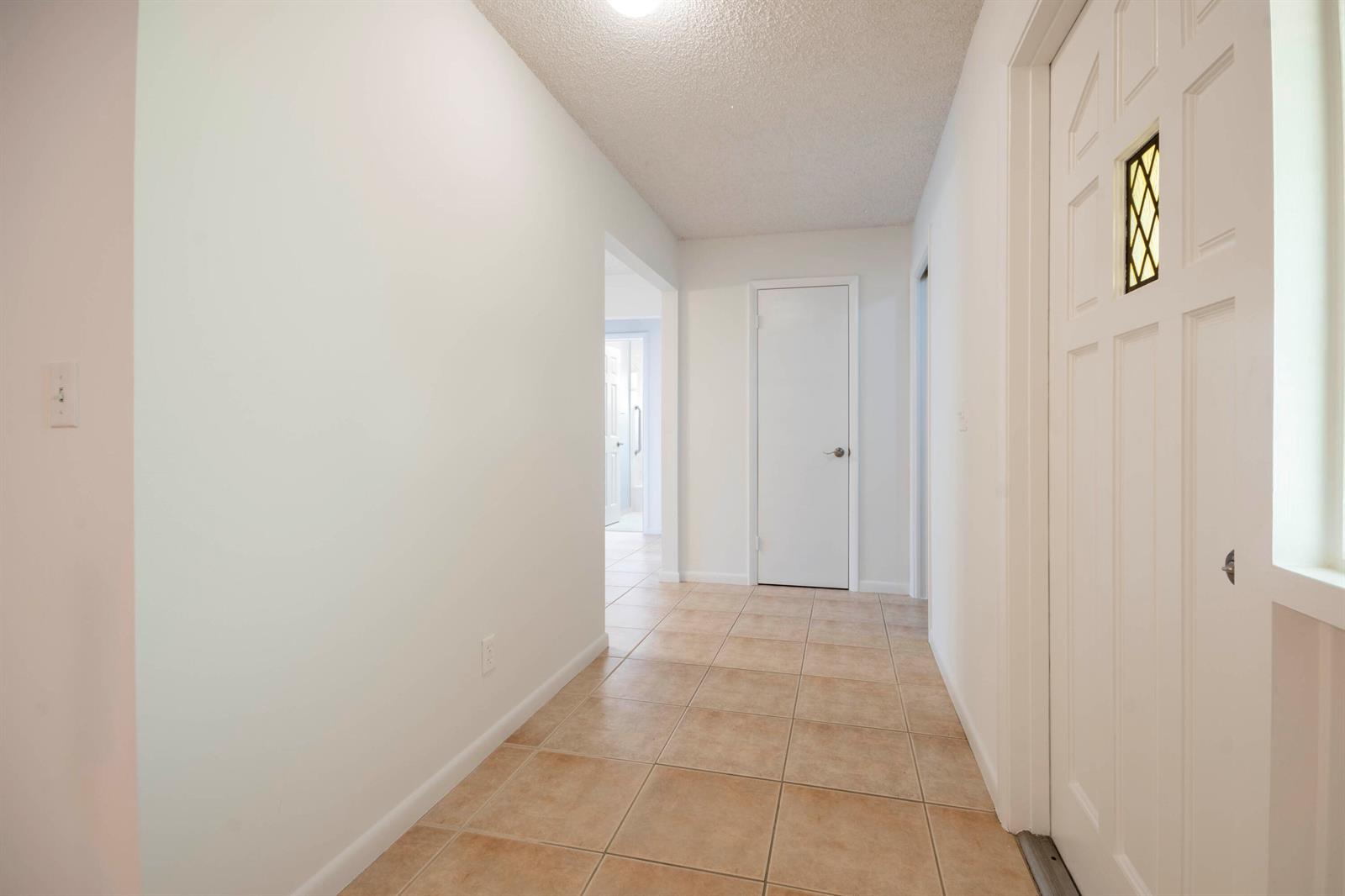 A hallway with beige tile flooring, white walls, and a white door at the end — 18020 Palm Point Drive, Jupiter FL 33458, JUPITER, FL