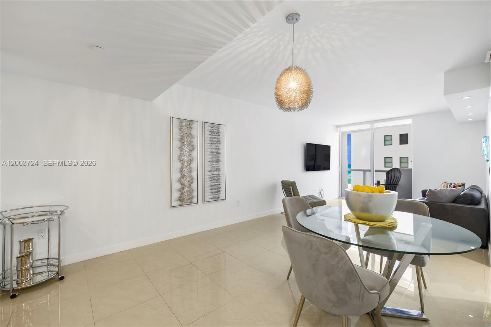 A dining area with a glass table, modern chairs, and a silver pendant light fixture — 6365 Collins Ave # 805, Miami Beach FL 33141, MIAMI BEACH, FL