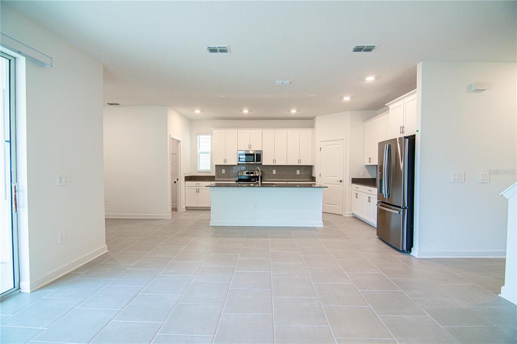 A modern kitchen features white cabinetry, stainless steel appliances, a center island, and tiled flooring — 3106 PARK VALE ROAD, ST CLOUD, FL