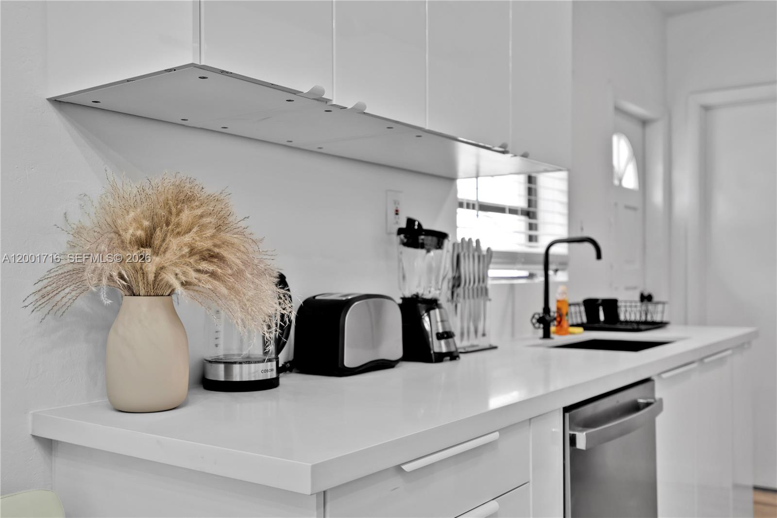 A modern white kitchen features a quartz countertop, black appliances, and a vase of pampas grass — 1510 Normandy Dr # A, Miami Beach FL 33141, MIAMI BEACH, FL