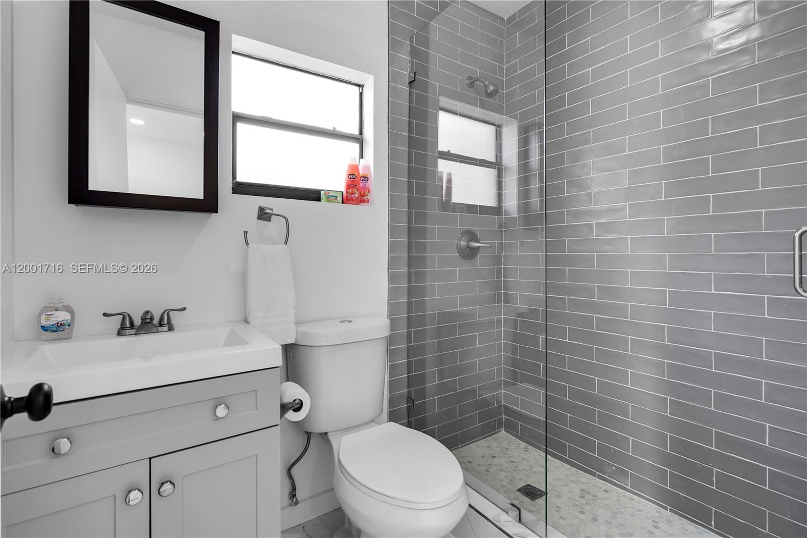 A bathroom features a gray vanity, a toilet, and a glass-enclosed shower with gray tiles — 1510 Normandy Dr # A, Miami Beach FL 33141, MIAMI BEACH, FL