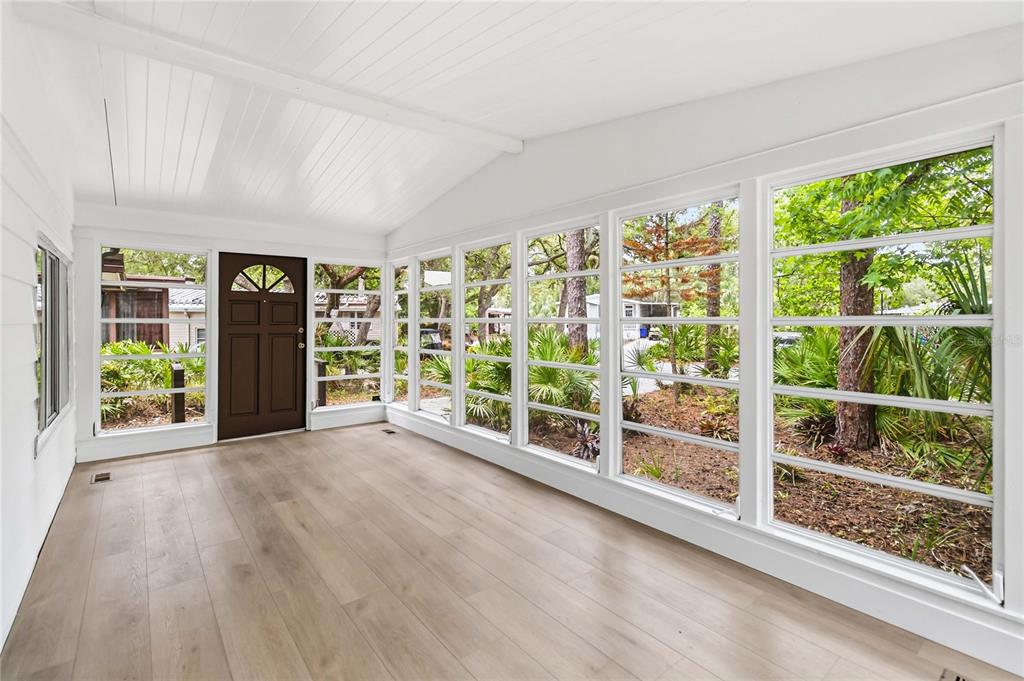 A sunroom with light wood-look flooring, white walls, and large windows overlooking a wooded area — 518 W PLANTATION BOULEVARD, LAKE MARY, FL