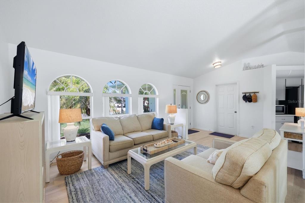 A bright living room features a vaulted ceiling, arched windows, and two beige sofas — 5981 MARIGOLD ROAD, VENICE, FL