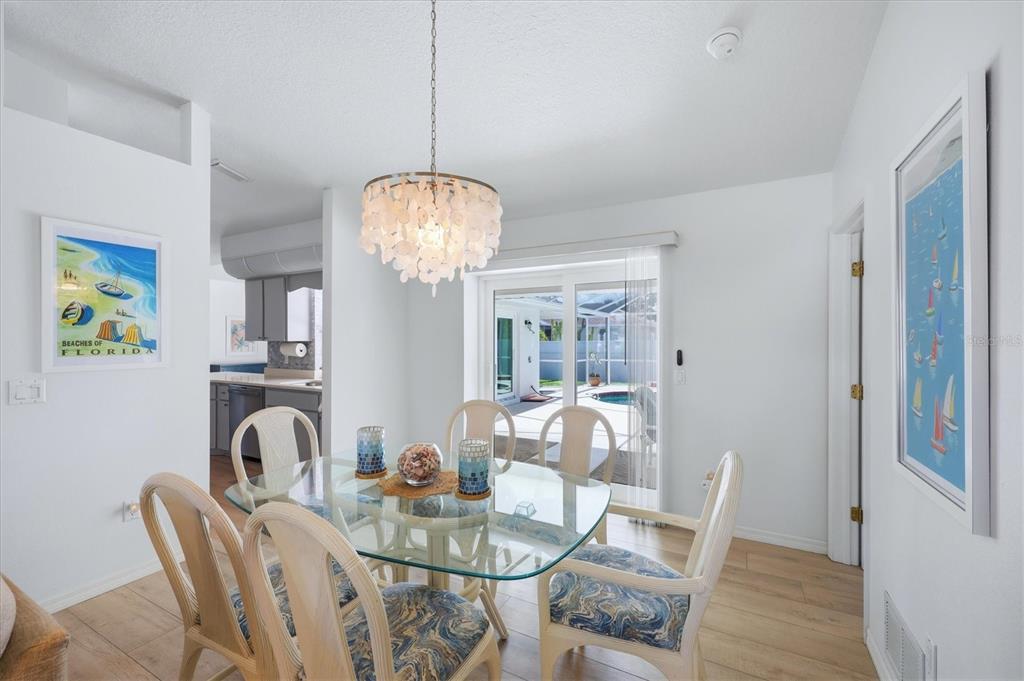 A dining room features a glass table, shell chandelier, and sliding doors to a pool — 5981 MARIGOLD ROAD, VENICE, FL