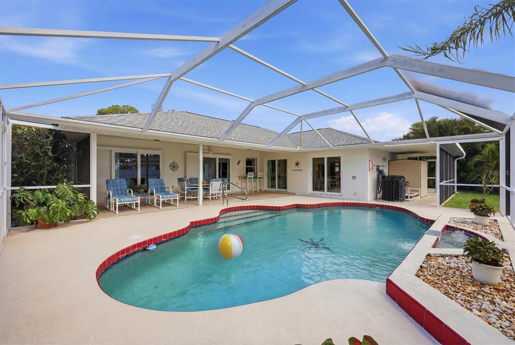 A swimming pool with a beach ball sits inside a screened-in patio behind a house — 5981 MARIGOLD ROAD, VENICE, FL
