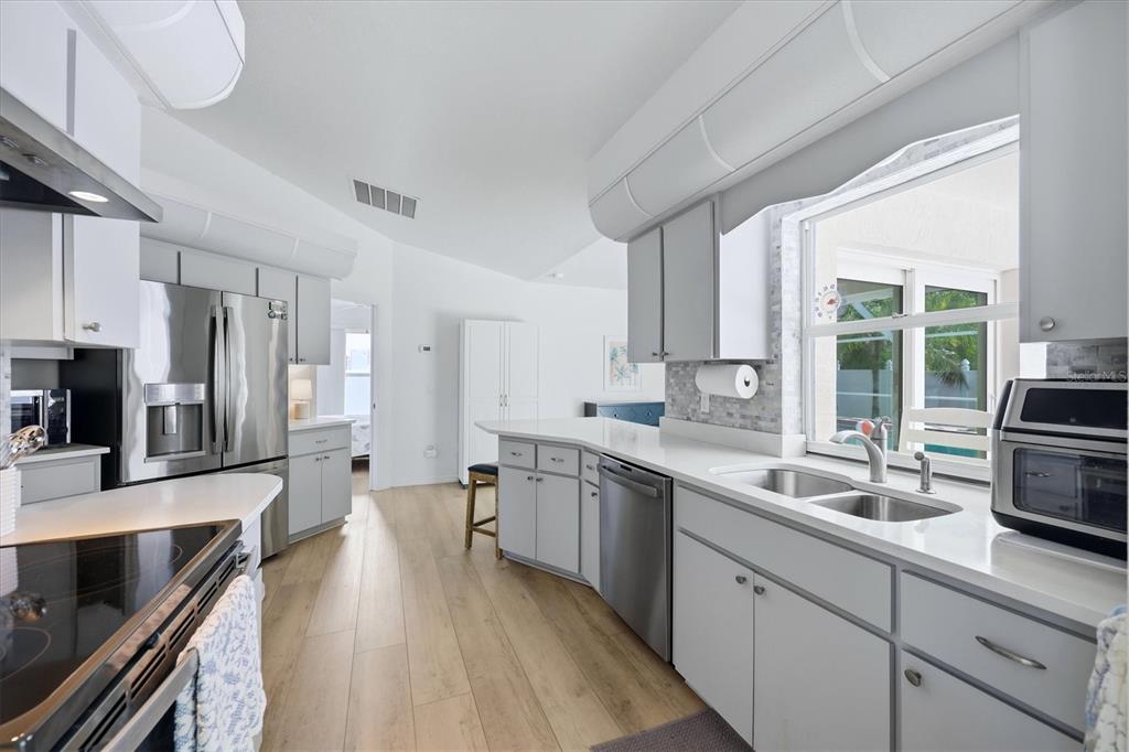 A bright kitchen features white cabinets, stainless steel appliances, and light wood-look flooring — 5981 MARIGOLD ROAD, VENICE, FL