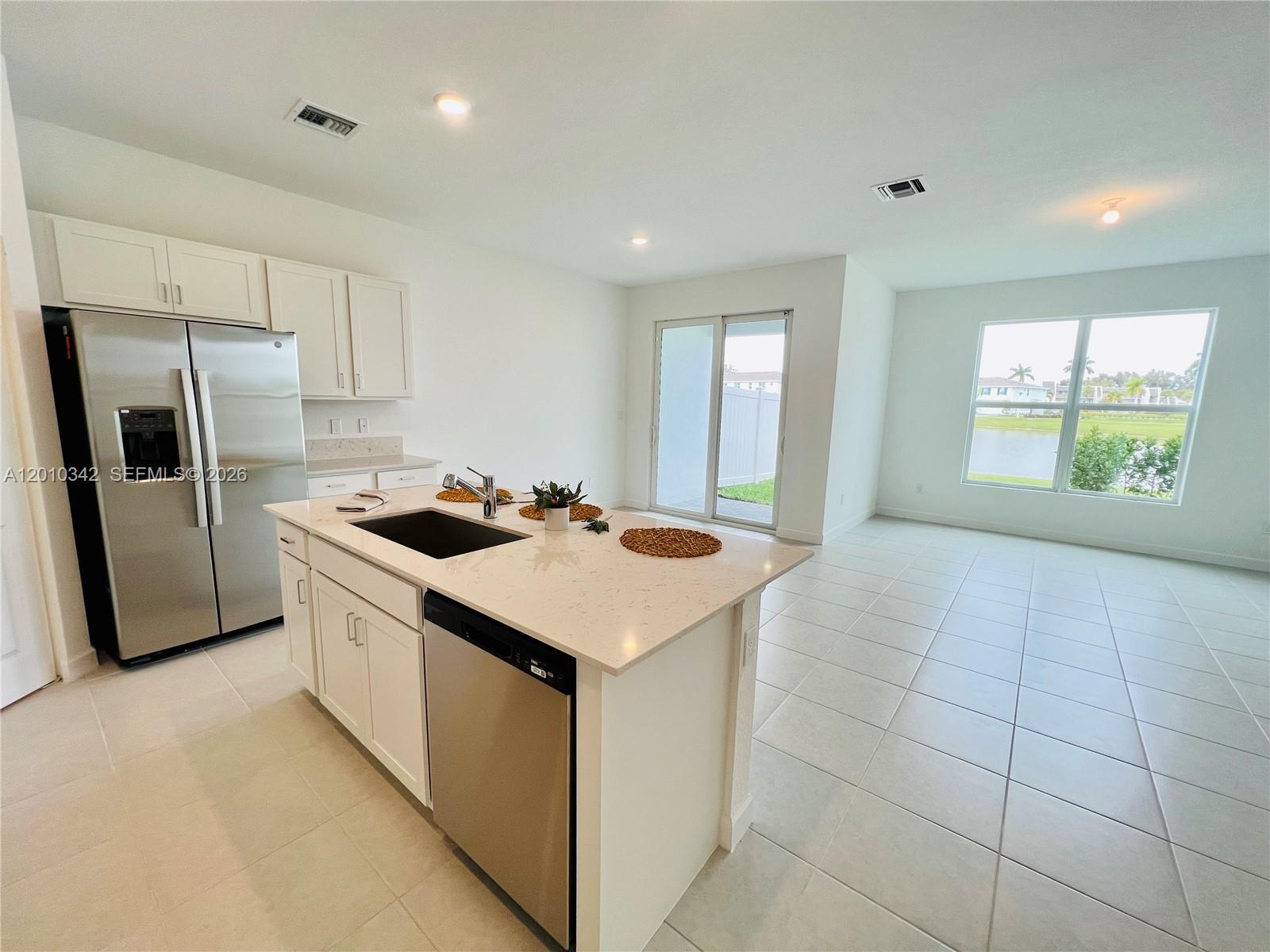 A modern kitchen with white cabinets, stainless steel appliances, and an island overlooks a lake — 6909 Harbours Edge Ave # 6909, Lake Worth FL 33467, LAKE WORTH, FL