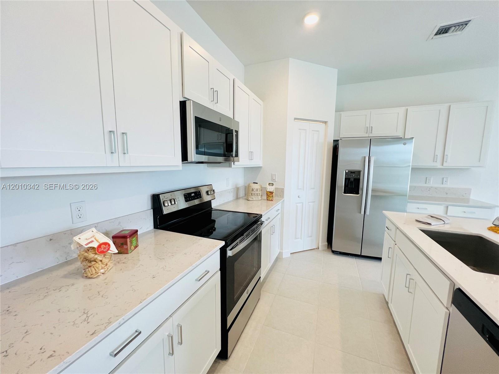 A modern kitchen features white cabinets, stainless steel appliances, and light-colored quartz countertops — 6909 Harbours Edge Ave # 6909, Lake Worth FL 33467, LAKE WORTH, FL