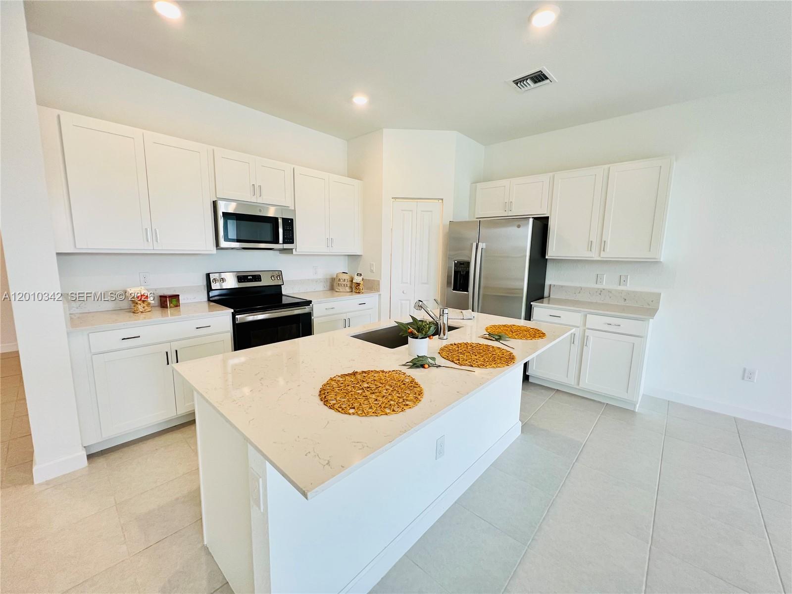 A modern kitchen features white cabinets, stainless steel appliances, and a central quartz-topped island — 6909 Harbours Edge Ave # 6909, Lake Worth FL 33467, LAKE WORTH, FL