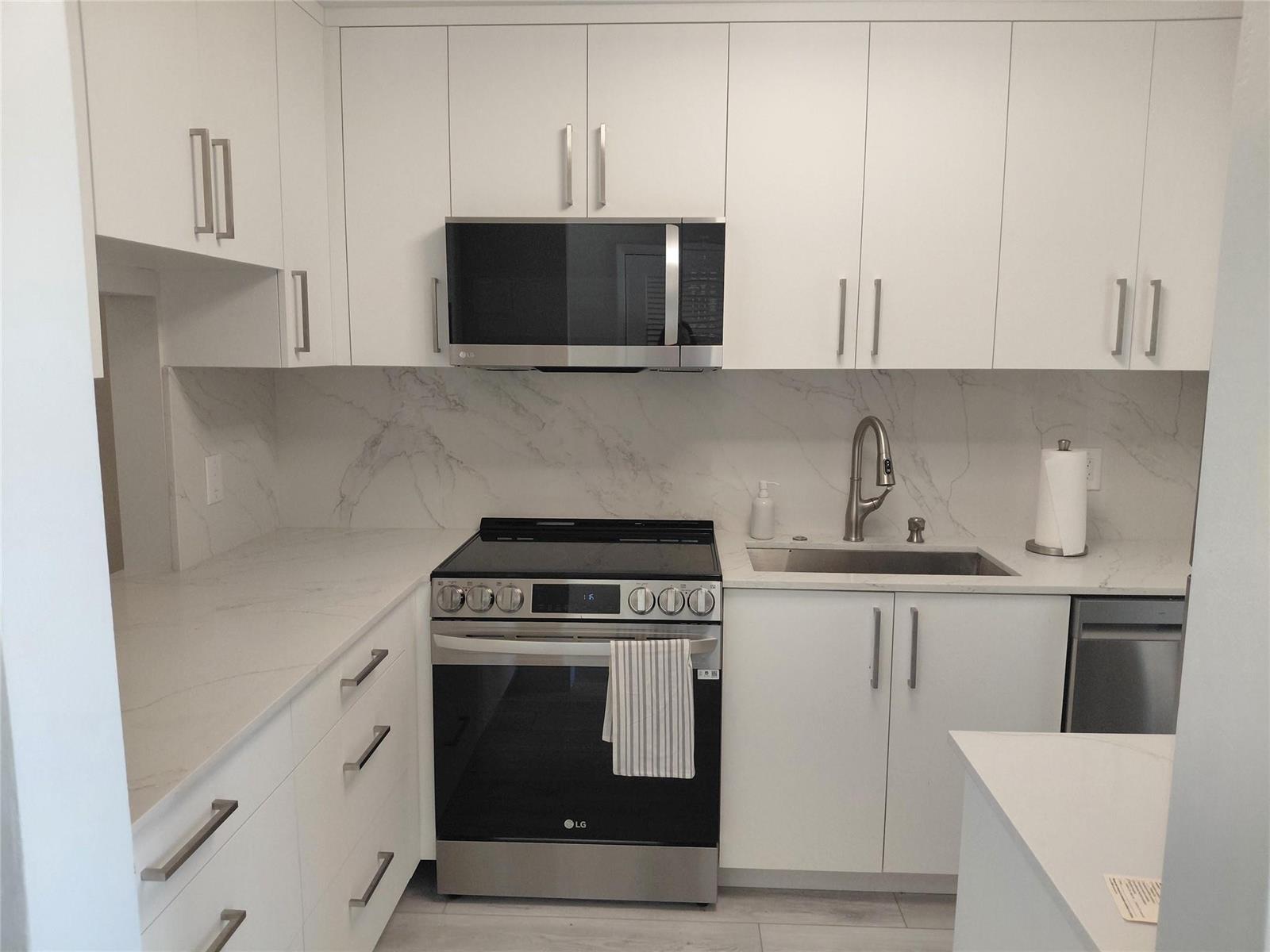 A modern kitchen featuring white cabinets, stainless steel appliances, and marble-patterned countertops and backsplash — 1951 NE 39th Street # 127, Lighthouse Point FL 33064, LIGHTHOUSE POINT, FL
