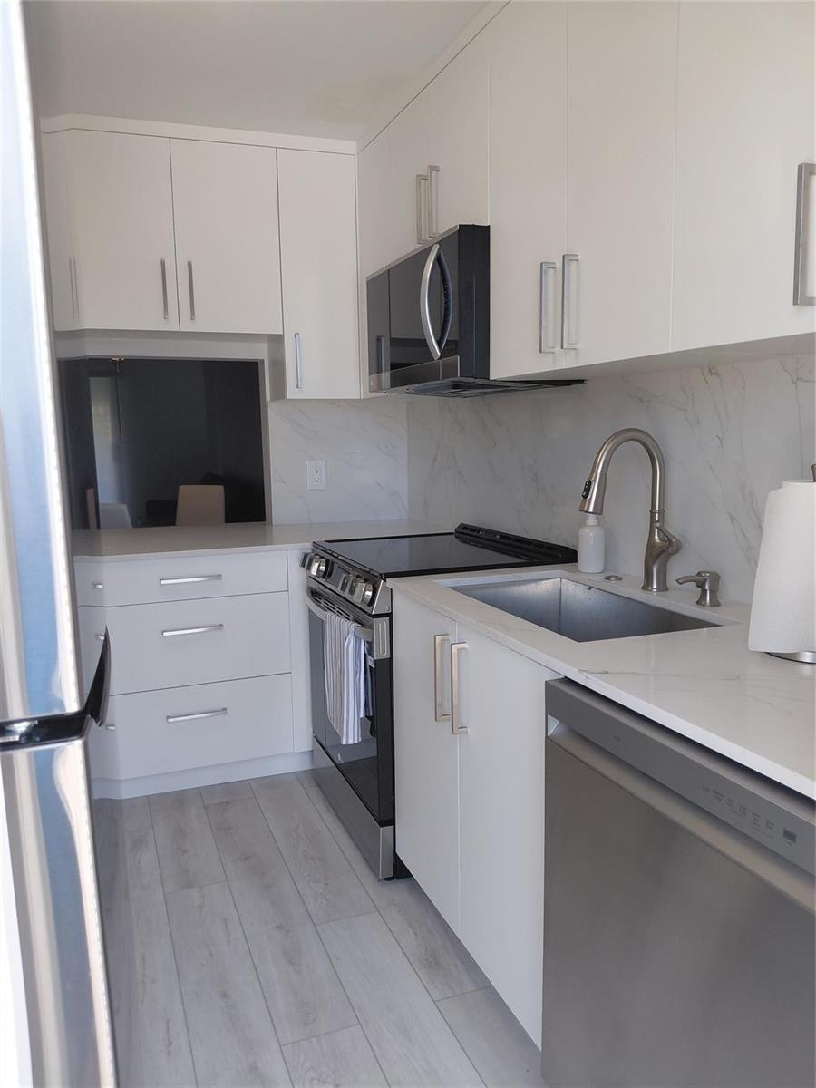 A modern kitchen features white cabinets, stainless steel appliances, and a marble-patterned backsplash — 1951 NE 39th Street # 127, Lighthouse Point FL 33064, LIGHTHOUSE POINT, FL