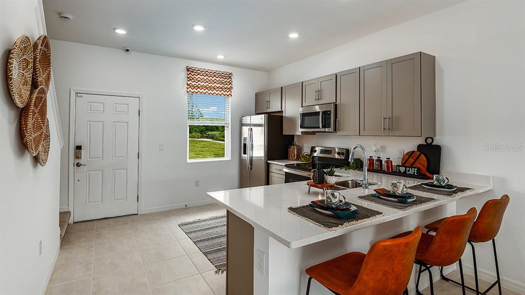 A kitchen features gray cabinets, stainless steel appliances, a quartz island, and three orange chairs — 10600 ORBIT TERRACE, SARASOTA, FL