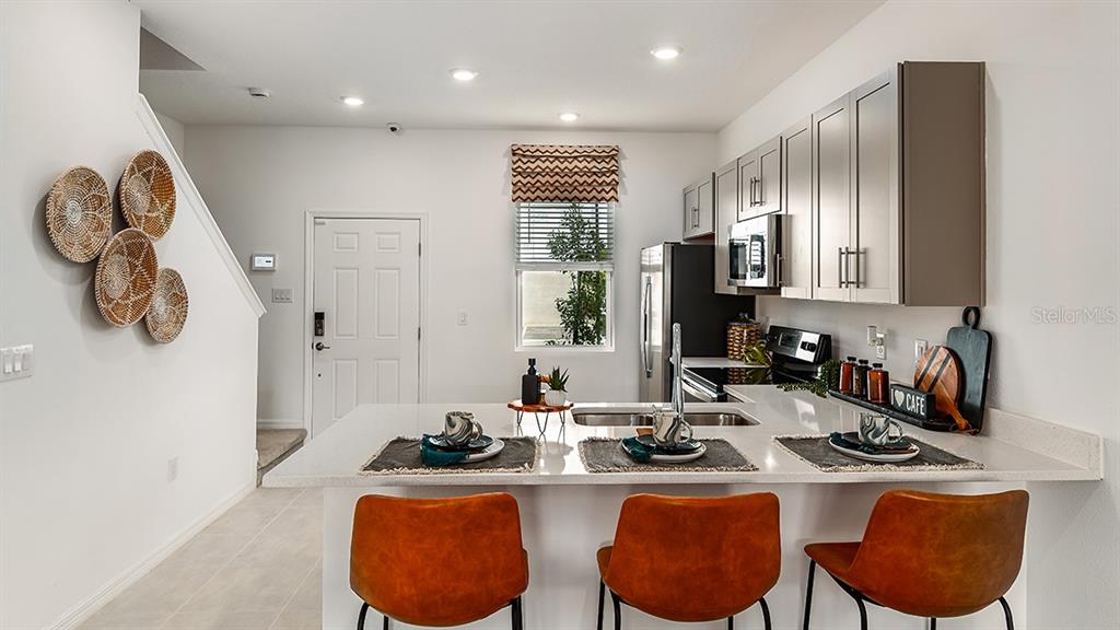 A modern kitchen features a breakfast bar with three orange chairs and gray cabinetry — 10600 ORBIT TERRACE, SARASOTA, FL